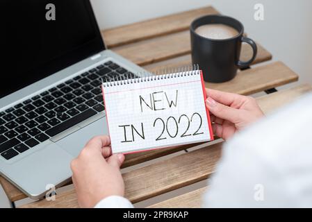 Insegna per scrittura a mano Novità nel 2022. Quest'anno è stato presentato un elenco di novità per l'approccio aziendale o la prossima donna d'affari che detiene un blocco note con un messaggio importante su Table with Lap Top. Foto Stock