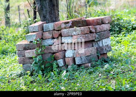 Pile di vecchi mattoni rossi di costruzione pesantemente usati parzialmente coperto con calcestruzzo preso dal vecchio muro di casa di famiglia suburbana ed accatastato ordinatamente Foto Stock