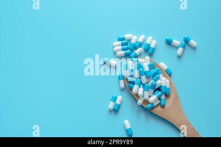 Pillole blu-bianche su cucchiaio di legno. Capsule pillole su sfondo blu. Argomenti di salute. Farmaco per malattia terapeutica. Uso di farmaci. Cure mediche. Industria farmaceutica. Produzione di capsule pillole. Foto Stock
