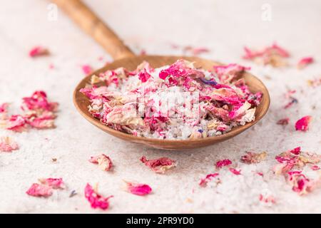 Vedi il wih di sale con petali di fiori secchi in paletta di legno sul tavolo di marmo rosa Foto Stock