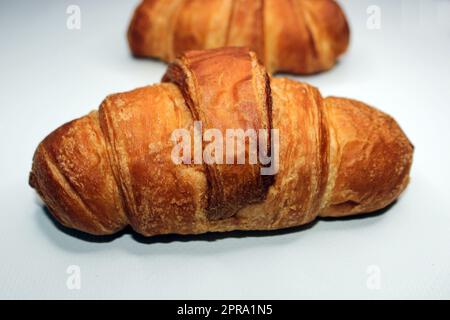 Croissant fresco e croissant in primo piano su uno sfondo chiaro. Croissant sfocato sullo sfondo. Cucinare, cucinare a casa Foto Stock