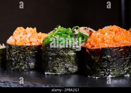 Primo piano di tre pezzi di sushi con diversi ripieni su un piatto nero. Foto Stock