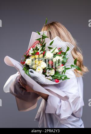 Donna in camicia bianca contiene un bouquet di fiori con rose, tulipani e verde. Foto Stock