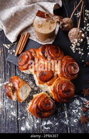 Ciambelle di cannella appena sfornate con spezie e farcitura con bevanda a base di caffè sul tavolo di legno. Foto Stock