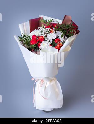 Fiori bianchi e rossi avvolti in carta floreale brillante su sfondo blu. Foto Stock