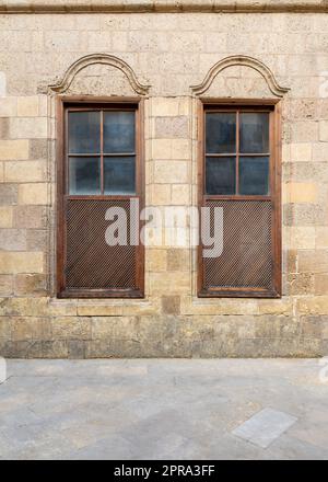 Vecchio muro in mattoni decorati in pietra abbandonata con due finestre ad arco in legno Foto Stock