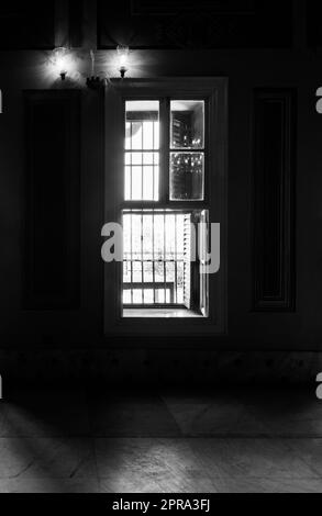 Bianco e nero di finestre strette, che rivelano una luce forte in una stanza buia con pavimento piastrellato in marmo Foto Stock