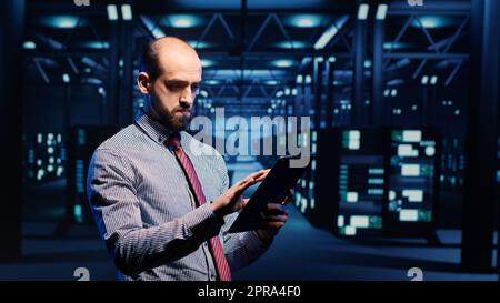 Responsabile della sicurezza delle informazioni che lavora nel data center con tablet, analizzando i cabinet dei rack dei server nella render farm. Specialista DEL supporto IT che ispeziona il sistema di cloud computing, ai Concept. Scatto con cavalletto. Foto Stock
