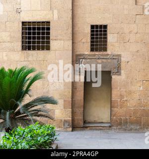 Antico muro esterno in mattoni decorati in pietra con due finestre e porta aperta Foto Stock