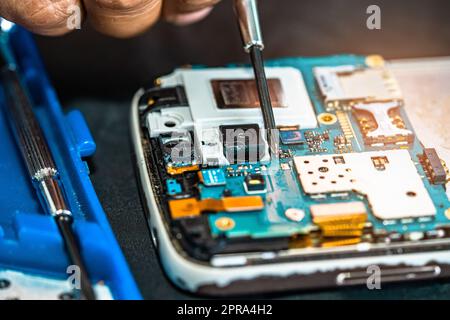 Tecnico che ripara l'interno del telefono cellulare mediante saldatore. Circuito integrato. Il concetto di dati, hardware, tecnologia. Foto Stock