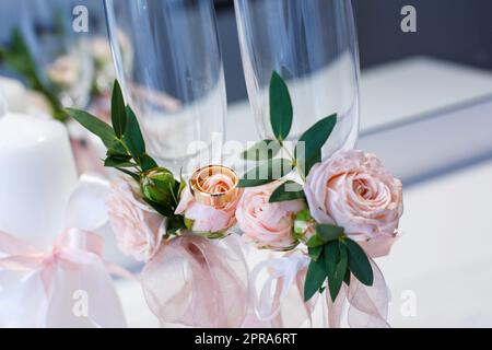 Due anelli nuziali dorati da vicino si trovano sui fiori che decorano i bicchieri da champagne. Foto Stock