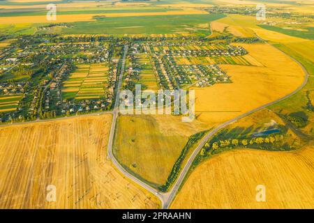 Vista aerea del villaggio e dei rulli di fieno, paesaggio dello Straw Field in serata d'estate. Pagliaio, rotolo di fieno in tempo di alba. Paesaggio agricolo di campagna nella stagione della vendemmia. Foto Stock