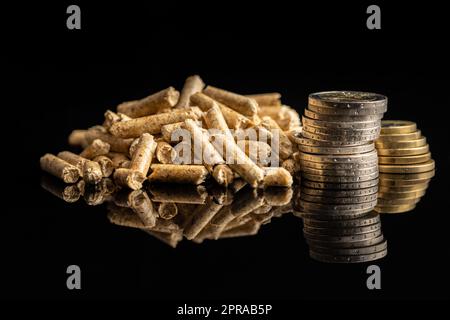 Pellet di legno e monete in euro su fondo nero. Biomassa Foto Stock