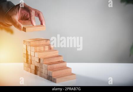 La mano di affari che organizza ha messo il processo di successo di crescita della scala del blocco di legno Foto Stock