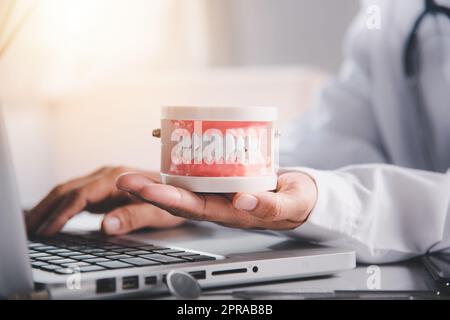 La dottoressa seduta e tenere il dente sulla scrivania presso l'ufficio clinico hanno un computer portatile Foto Stock