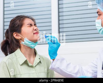 Medico uomo prendere il campione di saliva attraverso il naso con tampone di cotone per controllare il test di coronavirus da una giovane donna asiatica Foto Stock