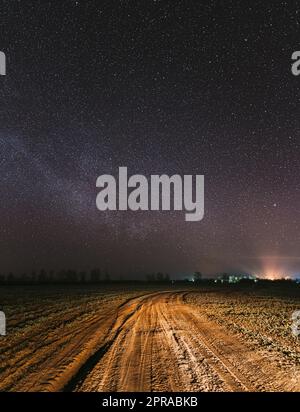 Notte Starry Sky con stelle incandescenti sopra campagna Road Landscape. La Via Lattea Galaxy e il prato rurale del campo Foto Stock