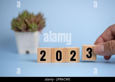 Mano uomo che tiene blocco di cubo di legno 2023 sullo sfondo. Foto Stock