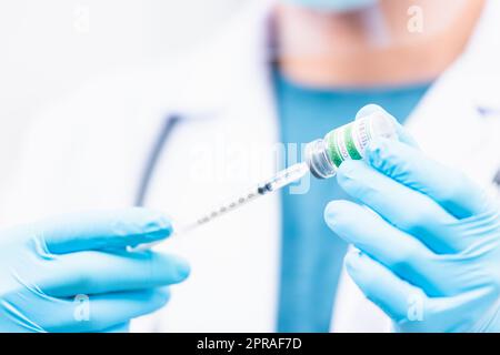Medico uomo siringa pull sul flacone liquido COVID-19 (coronavirus) vaccino per iniezione in ospedale Foto Stock