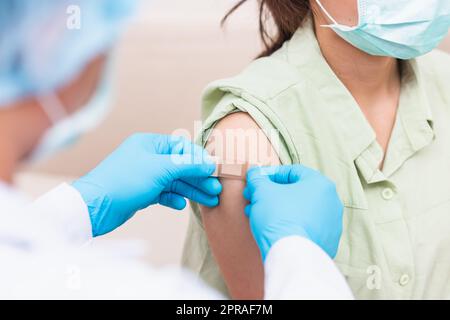 Medico uomo dopo iniezione vaccino contro il coronavirus alla spalla giovane donna che guanti protettivi di gomma mettendo un cerotto di benda adesiva Foto Stock