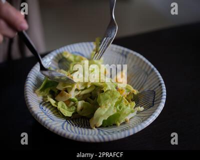 Donna che mescola deliziosi ingredienti per insalata alimentare con cucchiai in cucina Foto Stock