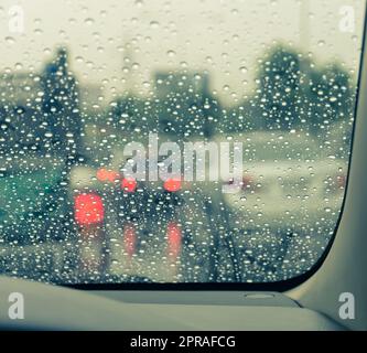 Sfocata vettura vista attraverso il parabrezza bagnato in giorno di pioggia Foto Stock