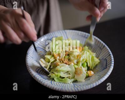 Donna che mescola deliziosi ingredienti per insalata alimentare con cucchiai in cucina Foto Stock