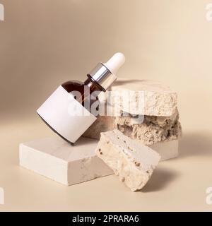 Flacone contagocce cosmetico marrone con etichetta vuota su pietre beige su primo piano giallo chiaro, Mockup Foto Stock