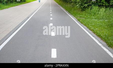 Primo piano di una strada asfaltata con linea di demarcazione intermittente e erba sul lato della strada. Messa a fuoco selettiva, fotografia in bianco e nero Foto Stock