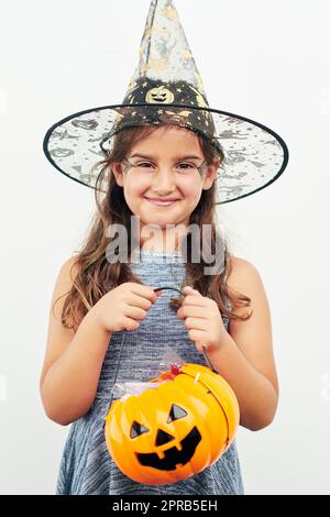 Pronta a fare il trick-or-treating. Una bambina che indossa un cappello di strega mentre tiene un jack o lanterna su uno sfondo bianco. Foto Stock