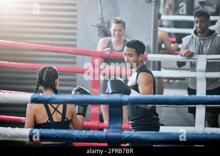 Due giovani pugili professionisti che si preparano a combattere e migliorare le loro abilità nel ring della boxe. Atleti forti e concentrati che si allenano insieme in palestra con gli amici che guardano da bordo campo. Foto Stock