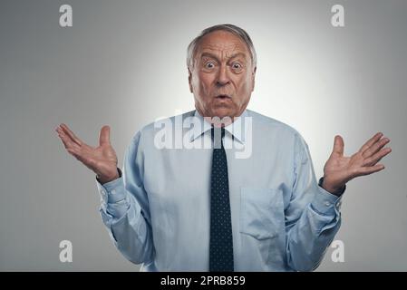 Che cosa state provando a dirmi: Un uomo d'affari anziano in piedi da solo su uno sfondo grigio nello studio e sembra confuso. Foto Stock