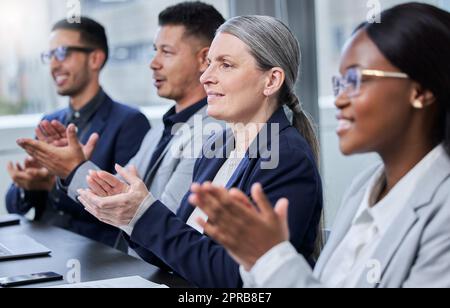 Il successo è sempre in grande mostra nella loro azienda. Una donna d'affari matura che applaude con i suoi colleghi durante una riunione in un ufficio. Foto Stock