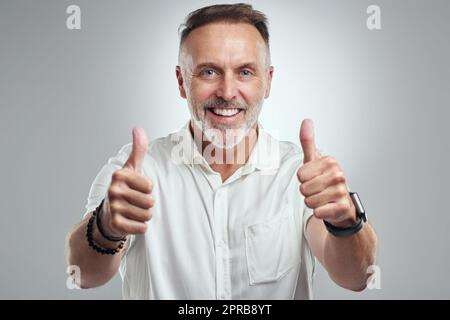 Sono così dannatamente orgoglioso di voi. Ritratto di studio di un uomo maturo che mostra i pollici su uno sfondo grigio. Foto Stock