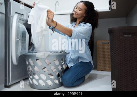 Questa polvere di lavaggio fa brillare i vestiti. Una giovane donna che si prepara a lavare un carico di lavanderia a casa. Foto Stock