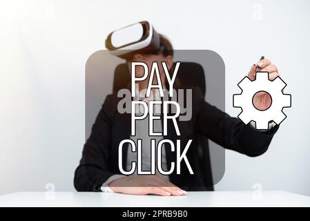 Segno di testo che mostra Pay per Click. Business idea modello di pubblicità Internet motore di ricerca strategia di marketing donna d'affari che indossa simulatore di realtà virtuale e tiene la penna alla scrivania. Foto Stock