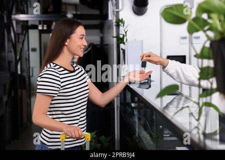 Felice giovane donna con valigia che riceve la chiave alla reception in ostello Foto Stock