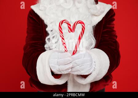 Babbo Natale che tiene canne caramelle su sfondo rosso, primo piano Foto Stock