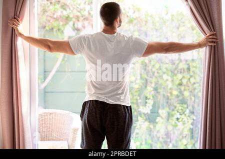 Mi piace aprire le tende a una giornata di sole, un giovane che apre la tenda al mattino in una giornata di sole. Foto Stock