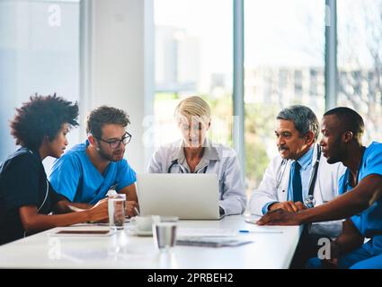 Team di medici che pianificano una riunione e fanno brainstorming in una sala riunioni utilizzando un computer portatile per leggere le note. Gruppo di operatori sanitari che discutono e parlano in un ufficio moderno Foto Stock