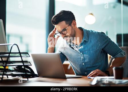 Uomo d'affari che soffre di mal di testa o emicrania a causa dello stress causato dalle scadenze di lavoro. Tenendosi a testa in mano, si sente ansioso, sopraffatto e stressato mentre si trova impegnato sulla scrivania del computer Foto Stock