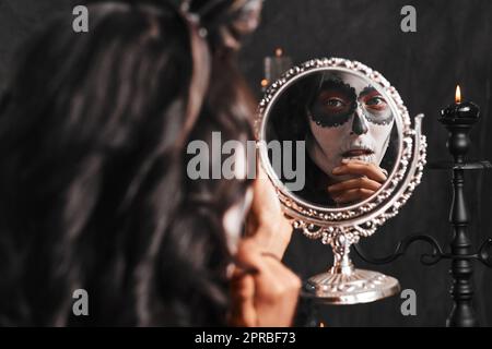 Halloween è arrivata. Una giovane donna attraente vestita con il suo costume di Halloween messicano che guarda in uno specchio. Foto Stock