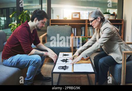 Un modello di inchiostro che determina il tuo modello di pensiero. Uno psicologo maturo che conduce un test di inkblot con il suo paziente durante una sessione terapeutica. Foto Stock