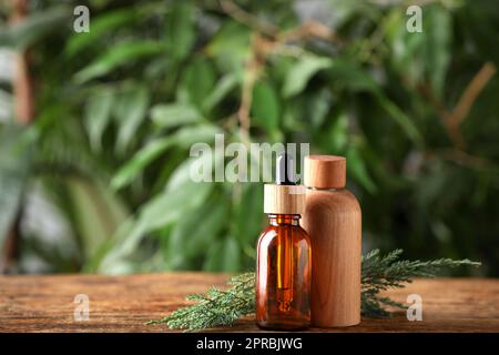 Bottiglie di olio essenziale di ginepro e rametti su tavola di legno su sfondo sfocato. Spazio per il testo Foto Stock