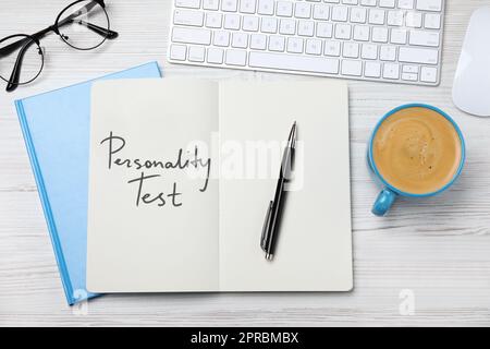 Notebook con testo Personality Test, tastiera per computer e tazza di caffè su scrivania di legno bianco, piano Foto Stock