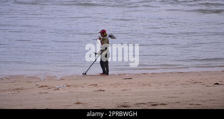 Una persona utilizza un metal detector per cercare in spiaggia monete o oggetti di metallo di valore durante la bassa marea a Jomtien, Pattaya, Thailandia. Foto Stock