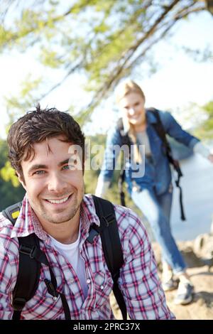Sono arrivato in cima per primo. Un bel giovane escursionista in attesa che la sua ragazza finisca di salire sulla montagna. Foto Stock