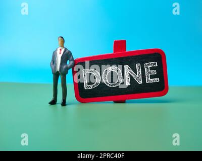 Persone in miniatura e tavola colorata con la parola FATTO. Foto Stock