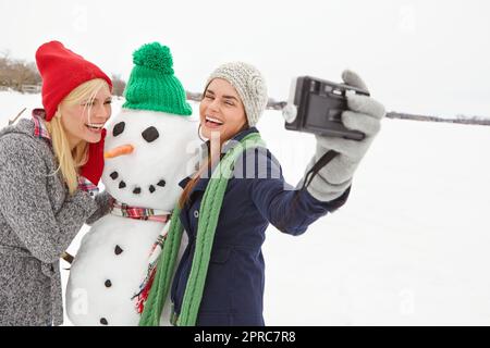 Tre migliori amici che fanno i ricordi. due bellissime giovani donne che prendono un selfie con un pupazzo di neve. Foto Stock