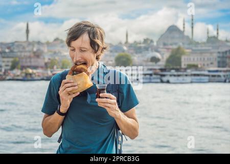 Uomo a Istanbul che fa colazione con Simit e un bicchiere di tè turco. Bicchiere di tè turco e bagel Simit contro la baia del corno d'oro a Istanbul Foto Stock